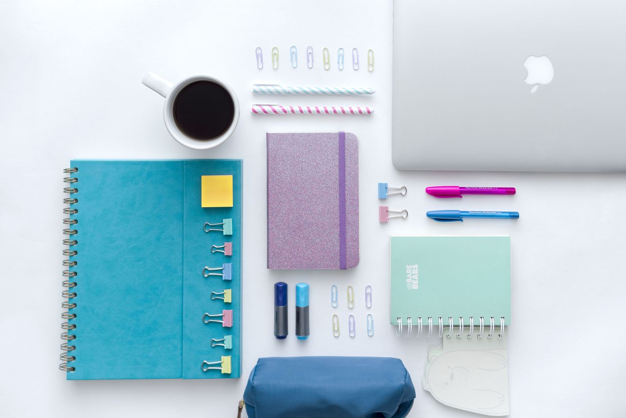 Flat lay of a colorful and organised office desk setup with notebooks, pens, and a laptop.